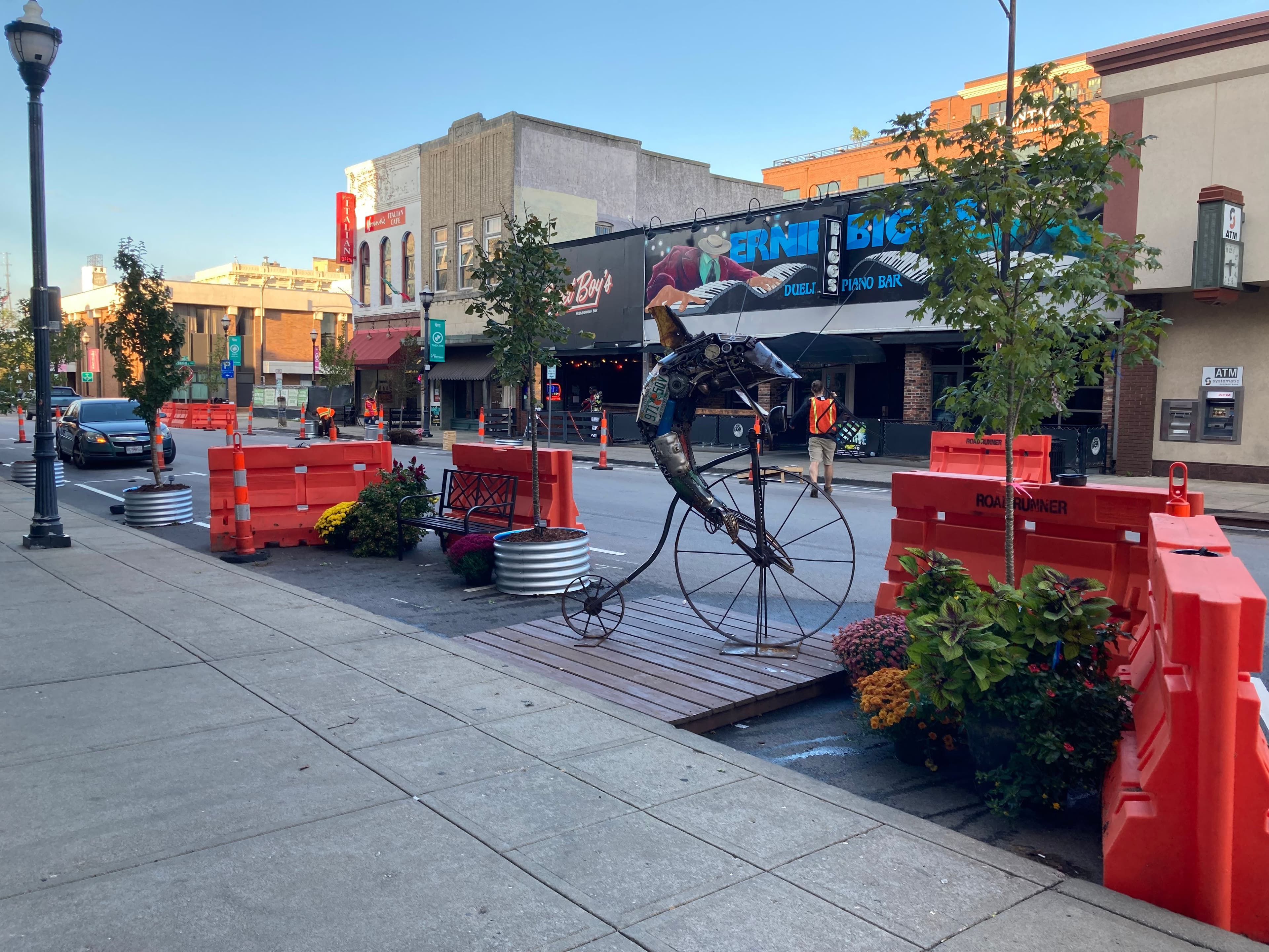 Image of a sculpture of a dolphin on a bike, trees, and a temporary cross-street walkway on South Avenue.