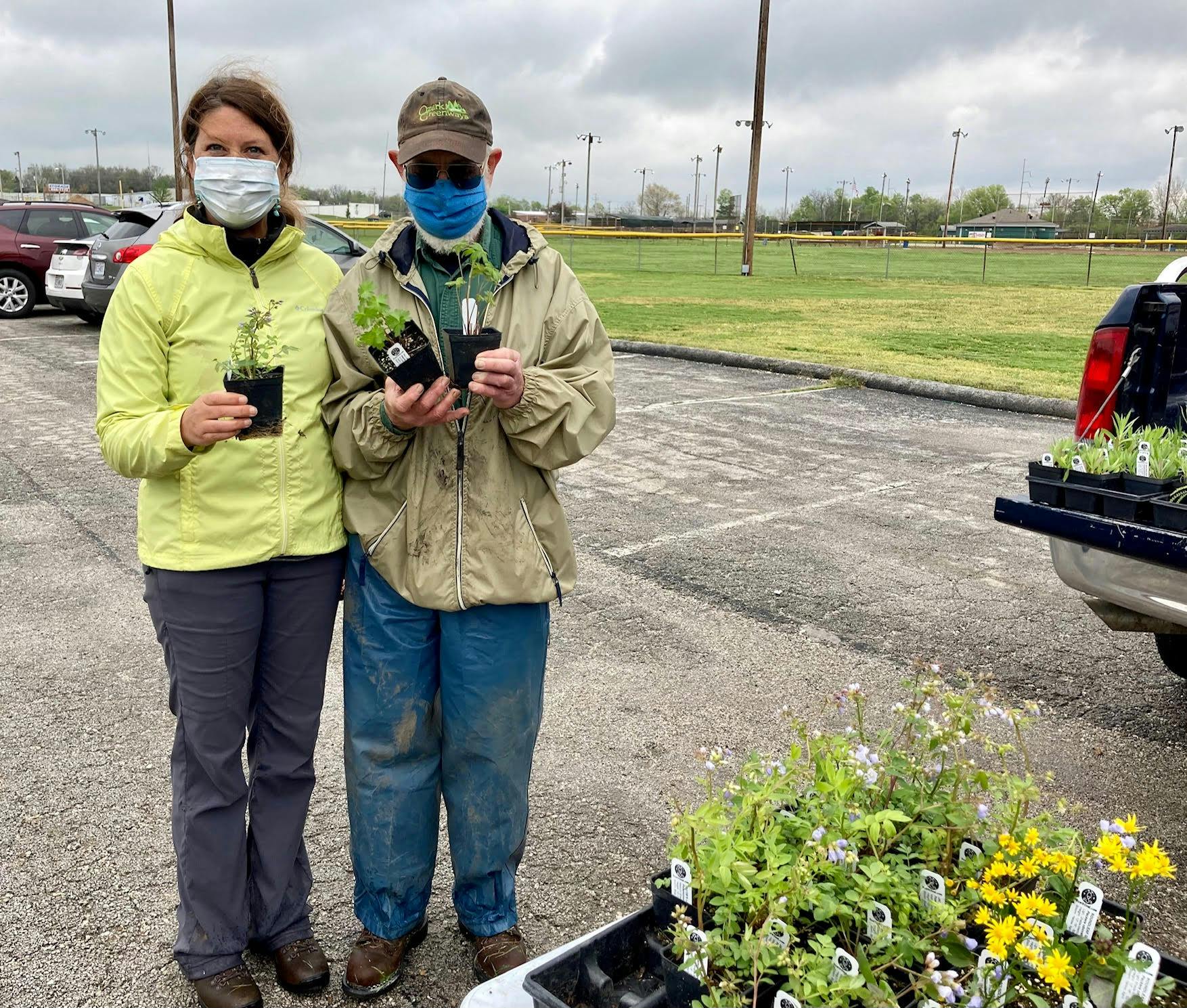 Image of two people wearing masks and holding plants to be planted around the community.